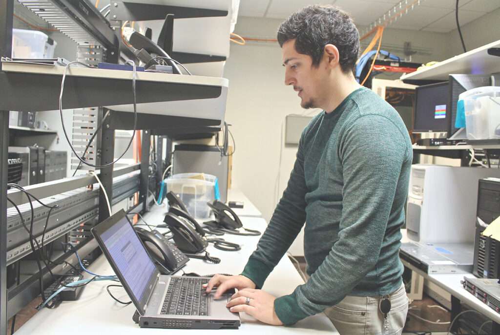 an information technology leader works on a laptop in a server room