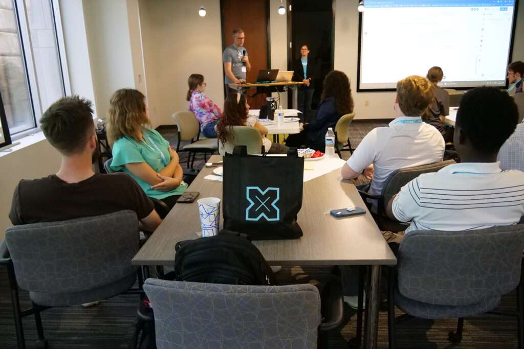 xterns listen intently to a presenter discussing the hackathon competition