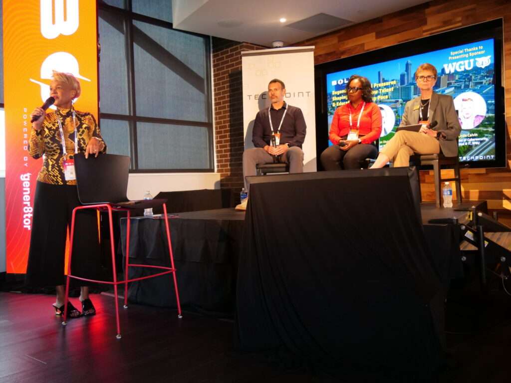 Moderator Linda Calvin speaks to the audience during a TechPoint BOLT Conference panel, powered by gener8tor. Seated on stage are Raman Ohri, Nicole Heatly-Holmes, and Carol Smith, discussing how organizations can adapt to rapid changes in technology and talent. The backdrop features BOLT and WGU branding with the Indianapolis skyline.