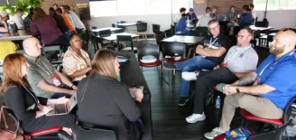 Attendees participate in a breakout discussion during the TechPoint BOLT Conference, powered by gener8tor. A small group of professionals sits in a circle sharing ideas, while other groups collaborate at nearby tables in the background. A “Breakout Session” sign is visible along the back wall.