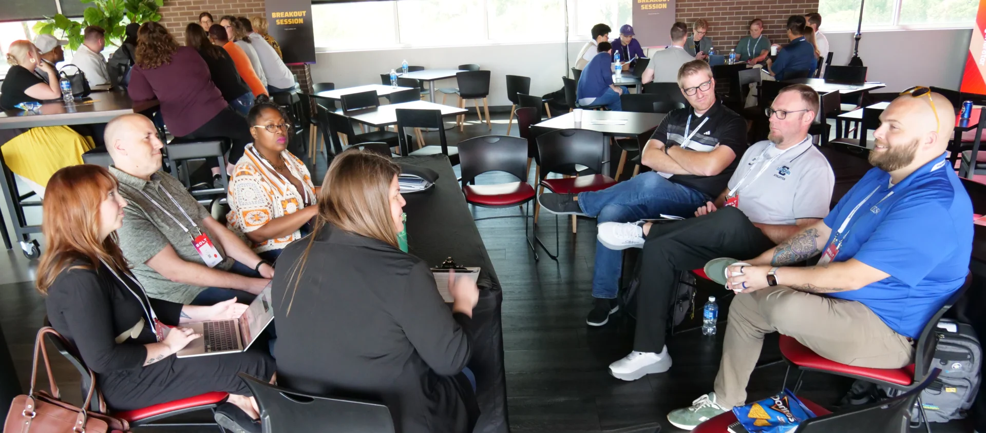Attendees participate in a breakout discussion during the TechPoint BOLT Conference, powered by gener8tor. A small group of professionals sits in a circle sharing ideas, while other groups collaborate at nearby tables in the background. A “Breakout Session” sign is visible along the back wall.