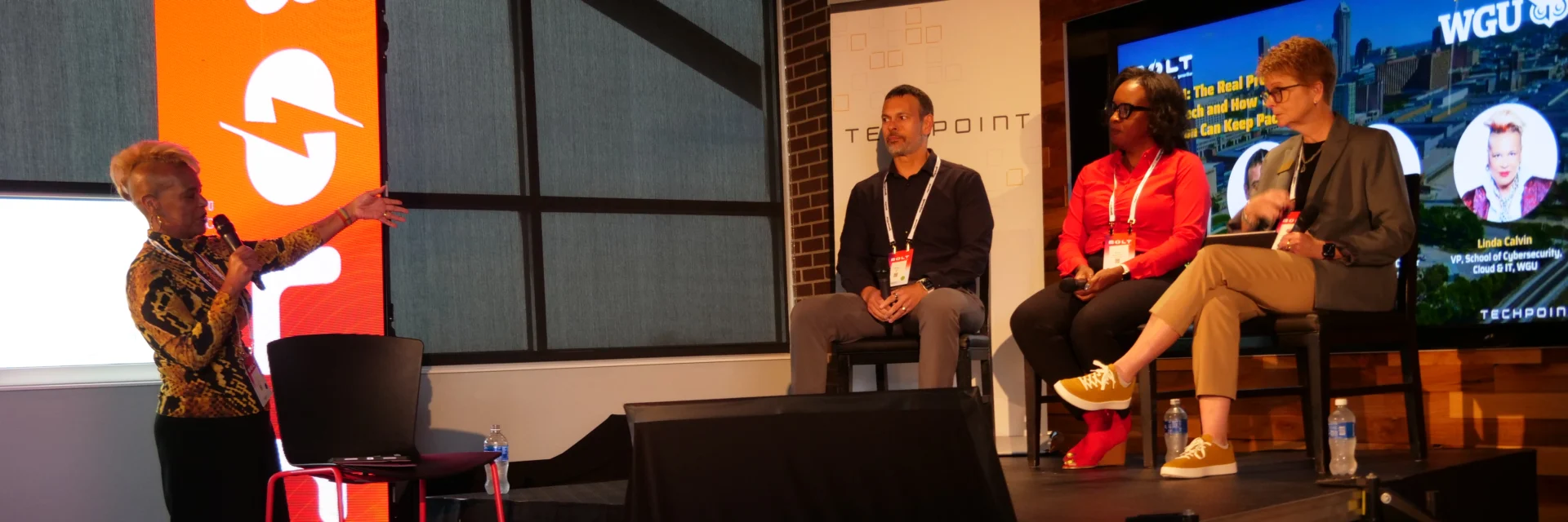 Moderator Linda Calvin leads a panel discussion at the BOLT Conference, powered by gener8tor and hosted by TechPoint. Three panelists sit on stage—Raman Ohri, Nicole Heatly-Holmes, and Carol Smith—discussing how organizations can adapt to rapid advances in tech and AI. A bright BOLT-branded display and WGU banner appear in the background.