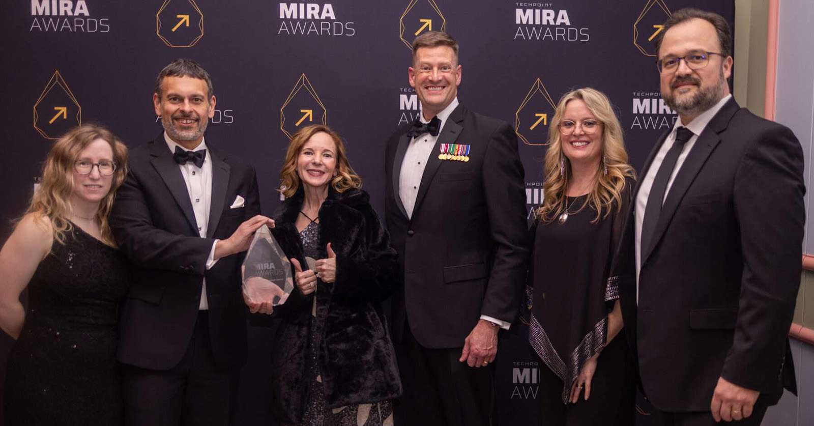 A group of six SEP team members stand together on the Mira Awards red carpet, dressed in formal attire and smiling as they hold the Exceptional Employer of the Year award.