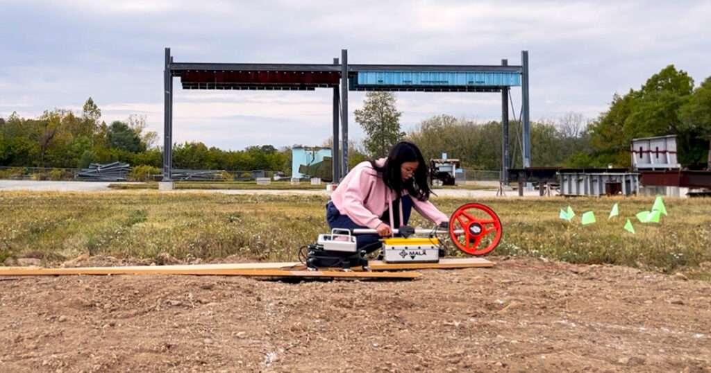 A woman in a pink sweater sets up an experiment in a field.