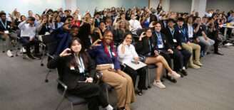 Students and organizers gather for a group photo during the 2026 Xtern Challenge at Cummins, with participants seated throughout the room making a “C” shape with their hands.