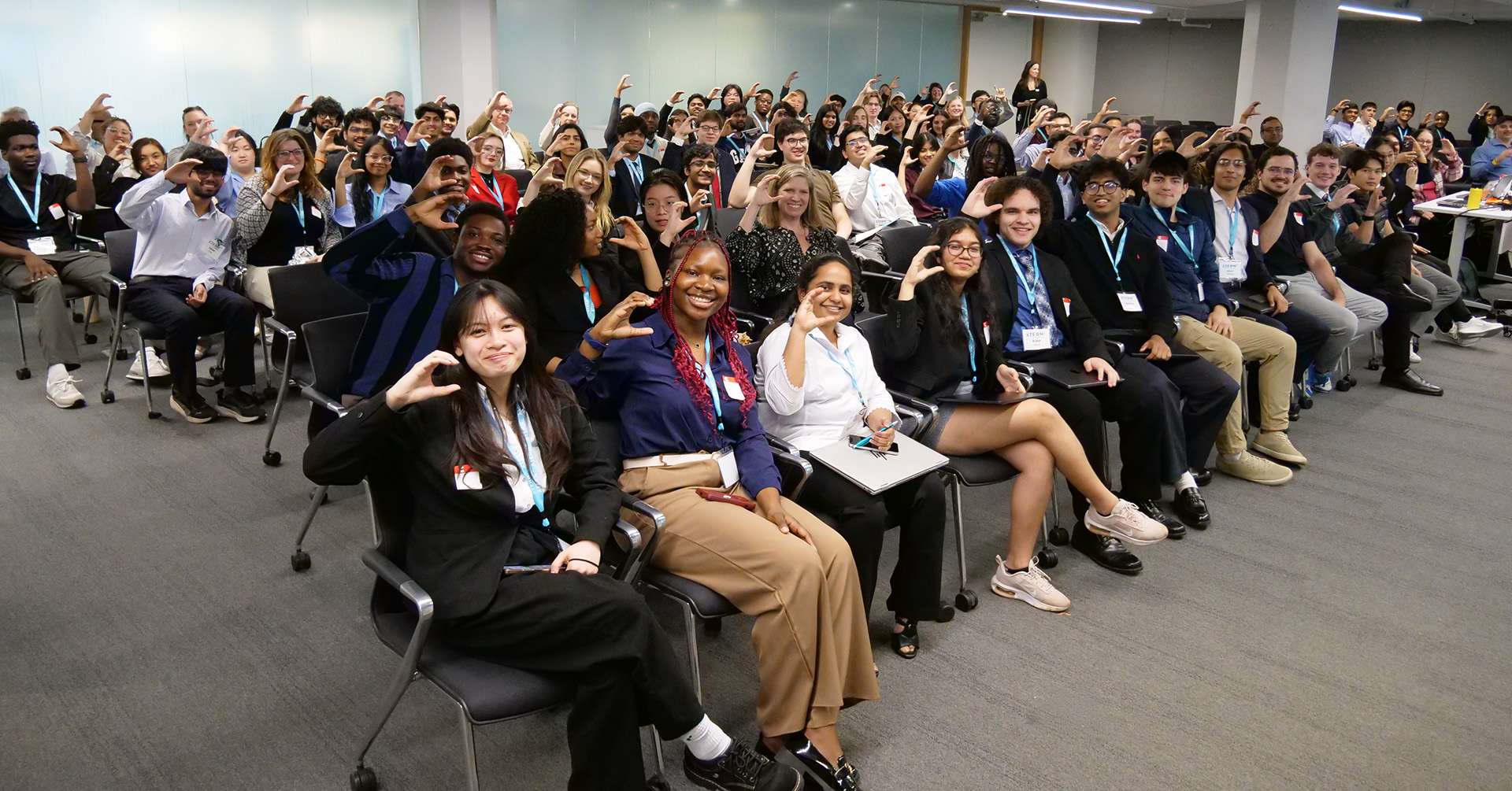 Students and organizers gather for a group photo during the 2026 Xtern Challenge at Cummins, with participants seated throughout the room making a “C” shape with their hands.
