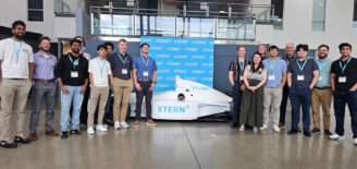 Sallie Mae team members and their Xterns pose in front of a white Xtern-branded IndyCar and blue Xtern backdrop at Dallara.
