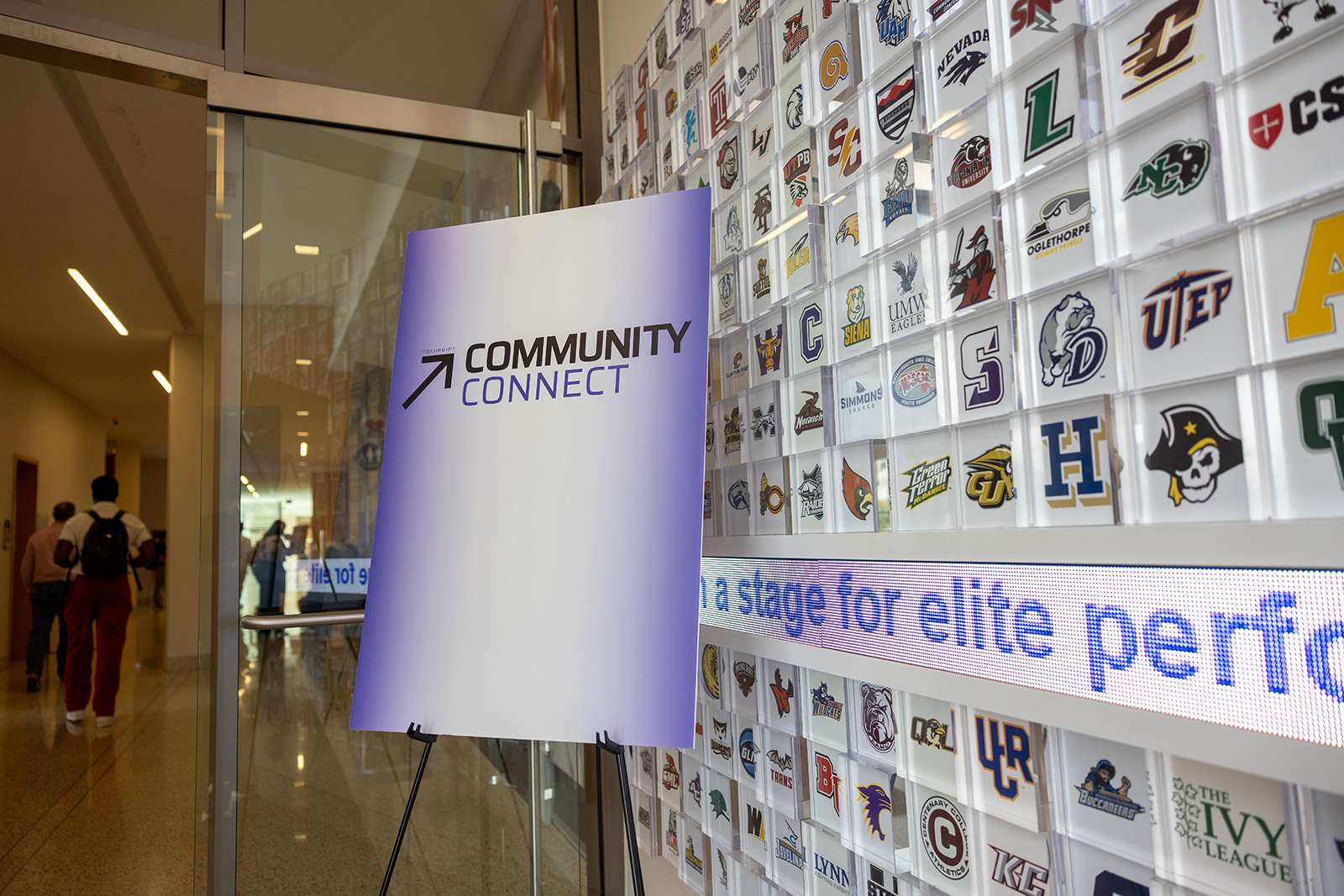 Community Connect signage stands inside the NCAA Hall of Champions beside a display featuring collegiate athletics logos.