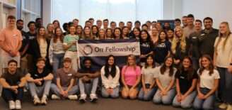 A large group of Orr fellows gather indoors, holding an Orr Fellowship banner.