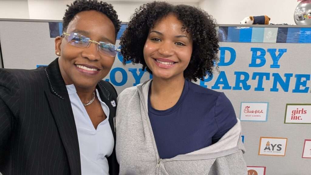 Dr. Carolyn Gentle-Genitty, founding dean of Founder's College, smiles for a selfie with a student in front of a board reading "Supported by Employer Partners," featuring logos including Chick-fil-A West Carmel, Girls Inc. and AYS At Your School.