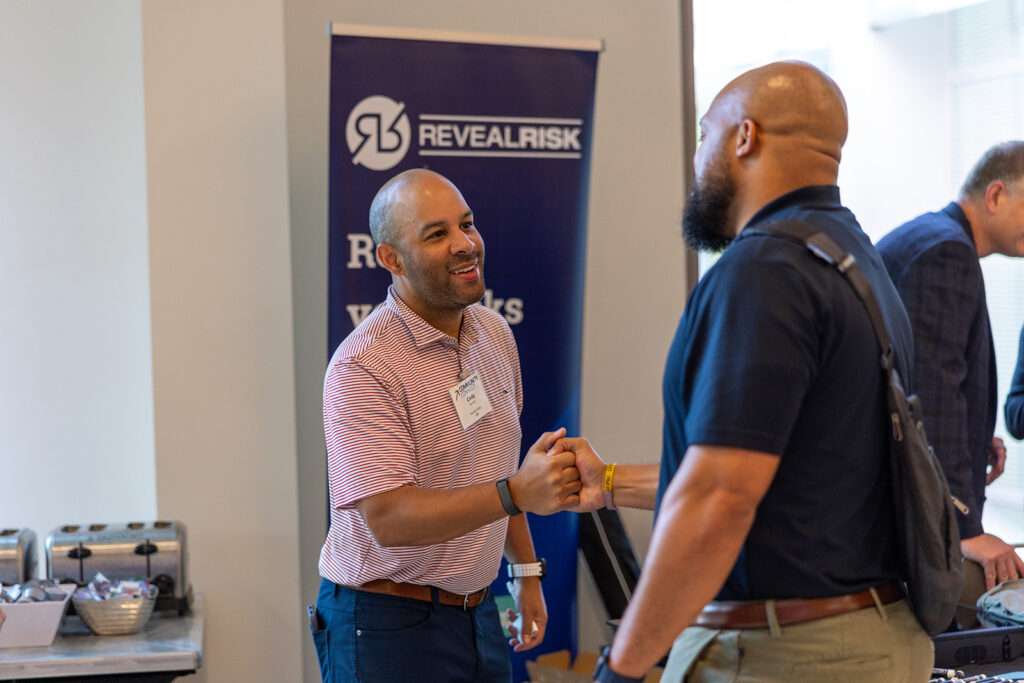 Cody Rivers of Reveal Risk shakes hands with an attendee beside the Reveal Risk booth at Community Connect.