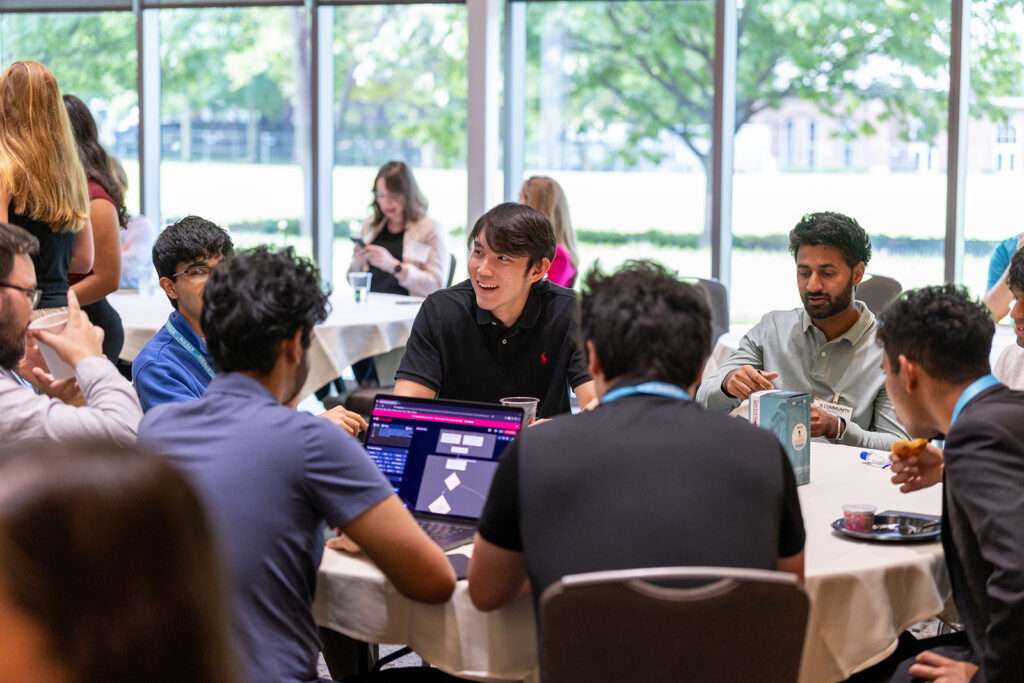 A mixed group of Community Connect attendees sits around a table during a discussion, with several participants wearing XTERN lanyards.
