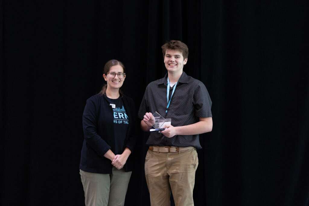 Patrick Green holds the 2026 XTERN Inclusion Award while posing with a TechPoint representative onstage.