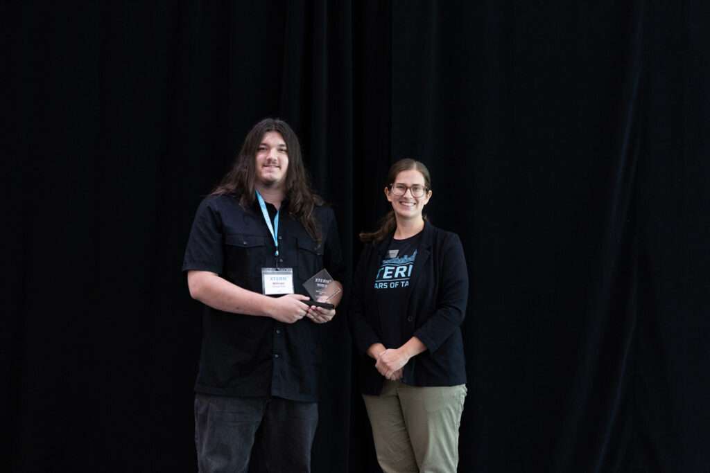 Will Daugherty holds the 2026 XTERN Investment Award while posing with a TechPoint representative onstage.