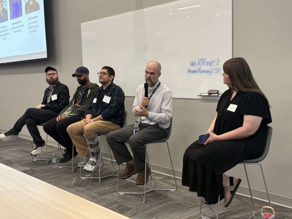 A panel of five speakers on stage, including TechPoint's Sally Reasoner, mid-discussion, with one panelist speaking into a microphone and a moderator listening at the far end.