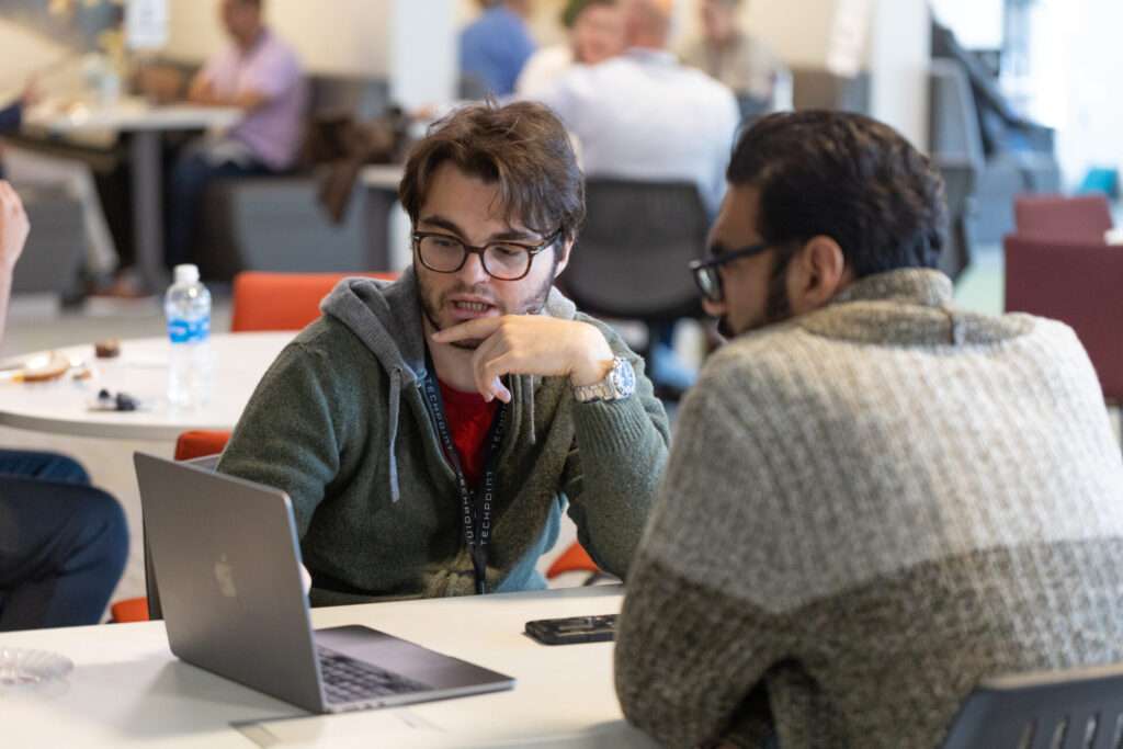 Two Venture Connect participants have a one-on-one conversation across a table with a laptop during a TechPoint event.