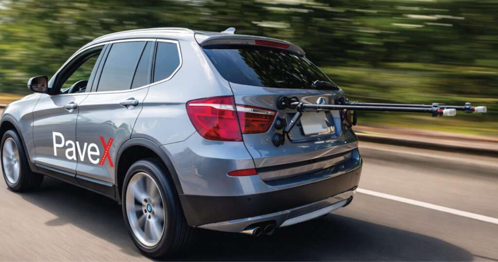 A car with the PaveX sensor system and logo drives on a road.