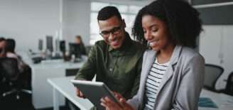 Two coworkers review information together on a tablet in a modern office.