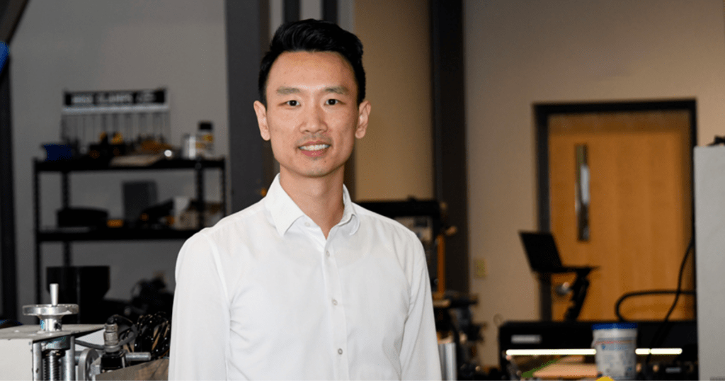 A Purdue researcher wearing a white dress shirt stands in an engineering laboratory and looks into the camera.