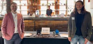 Michael Zwach and Azara Energy co-founder Justin Siples stand on either side of an Azara Energy display table featuring prototype electrical outlets and company materials.