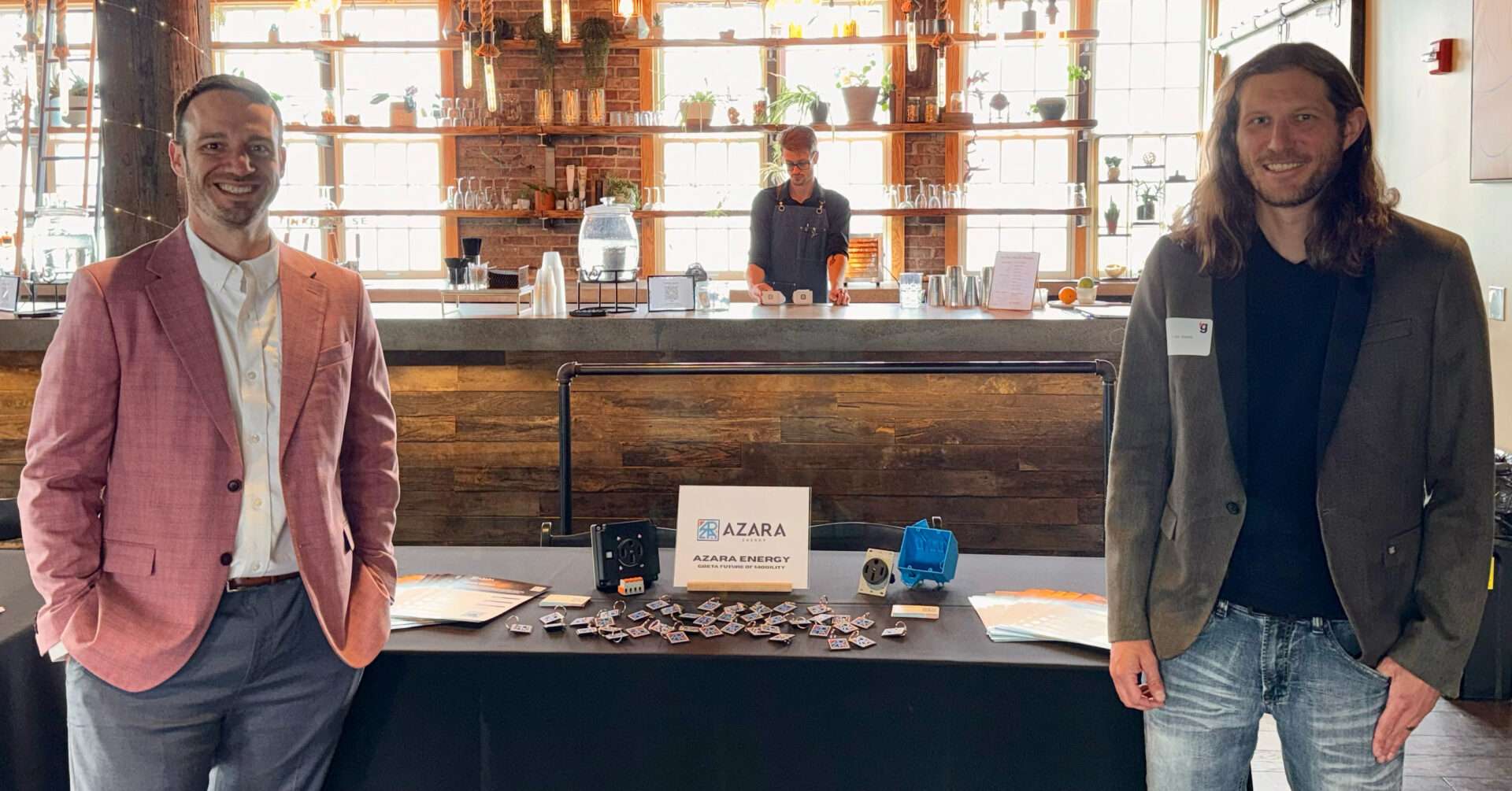 Michael Zwach and Azara Energy co-founder Justin Siples stand on either side of an Azara Energy display table featuring prototype electrical outlets and company materials.