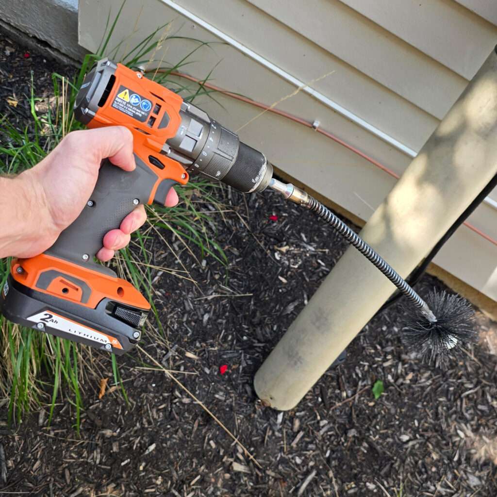A person holds a cordless drill fitted with a long vent-cleaning brush during a Crowfly customer ride-along.
